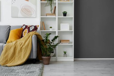 Oturma odasının içinde kanepe, raf ünitesi ve yapay bitkiler var.