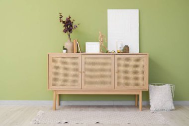 Yapay okaliptüslü vazo, kitaplar ve dekorlar yeşil duvarın yanındaki klozette.