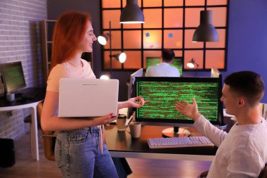 Dizüstü bilgisayarı olan bir kadın programcı ve gece ofiste çalışan bir meslektaşı.