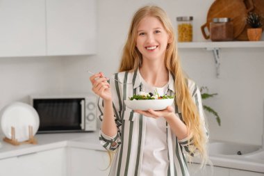 Mutfakta peynirli lezzetli salata tabağı tutan genç bir kadın.