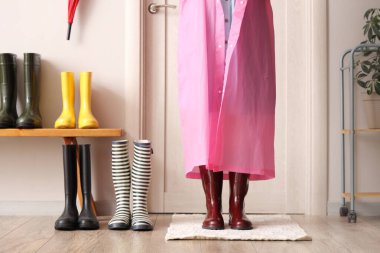 Koridorda farklı lastik çizmeleri olan yağmurluk giymiş güzel bir kadın.