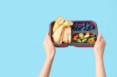 Kadın elleri ve mavi arka planda muz olan okul beslenme çantası.