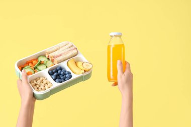 Okulun beslenme çantalı kadın elleri ve sarı arka planda bir şişe meyve suyu.