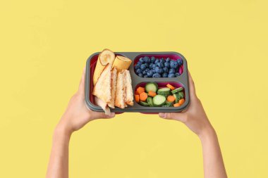 Kadın eli ve okul beslenme çantası. Sarı arka planda muz var.