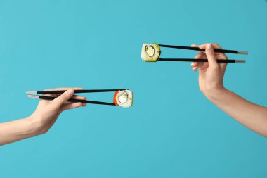 Dişi eller yemek çubuklarını tutarken mavi arka planda farklı lezzetli suşi dürümleri yapıyorlar.