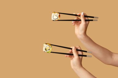 Kadın elleri, bej arka planda farklı lezzetli suşi ruloları olan çubukları tutuyor.