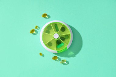 Turkuaz arka planda yuvarlak plastik hap organizatörü ve kapsüller. Üst görünüm