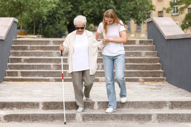 Kör büyükannesiyle parkta yürüyen genç bir kadın.