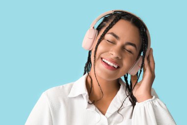 Genç Afro-Amerikalı kadın mavi arka planda müzik dinliyor.