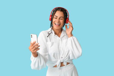 Mavi arka planda müzik dinleyen Afro-Amerikalı genç bir kadın.