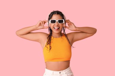 Genç Afro-Amerikalı kadın pembe arka planda müzik dinliyor.