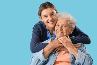 Hemşire mavi arka planda yaşlı kadına sarılıyor, yakın plan.