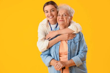 Hemşire sarı arka planda yaşlı kadına sarılıyor.