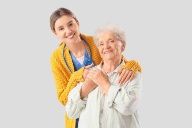 Hemşire arka planda yaşlı kadına sarılıyor.