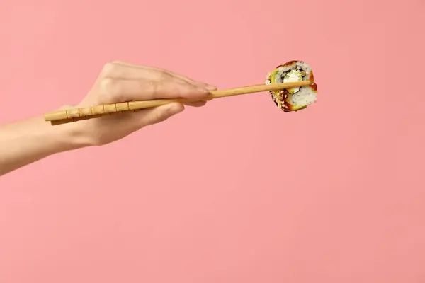 stock image Female hand holding chopsticks with tasty sushi roll on pink background