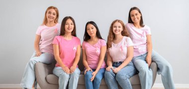 Bir sürü pembe kurdeleli kadın arka planda, koltukta oturuyor. Göğüs kanseri farkındalığı konsepti