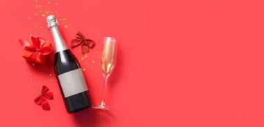 Bir şişe şampanya, cam, fiyonk ve kırmızı arka planda mesaj için yeri olan Noel hediyesi.