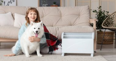 Young woman with plaid and Samoyed dog warming near radiator at home clipart