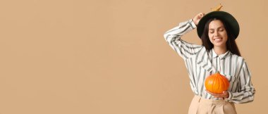 Bej arka planda taze balkabağı ve sonbahar yaprağı tutan zarif genç bir kadın.