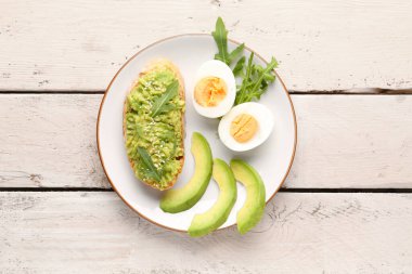 Hafif ahşap arka planda avokadolu lezzetli bir bruschetta tabağı.