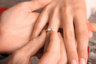 Erkek kadının parmağına nişan yüzüğü takıyor, yakın plan.