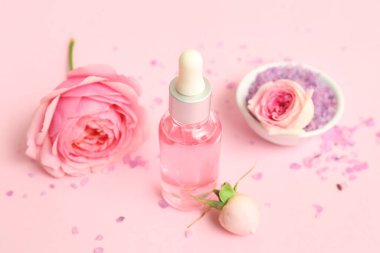 Gül özü ve pembe arka planda çiçekler olan bir şişe kozmetik yağı.