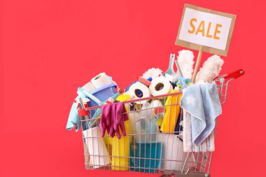 Kırmızı arka planda kelime satışı olan temizlik malzemeleriyle dolu bir alışveriş arabası.