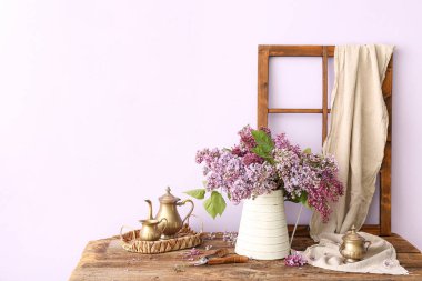 Vazoda leylak demeti ve duvarın yanındaki ahşap masada mutfak gereçleri.