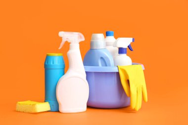 Turuncu arka planda farklı temizlik malzemeleri olan bir kase.