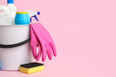 Pembe arka planda farklı temizlik malzemeleriyle dolu kova.