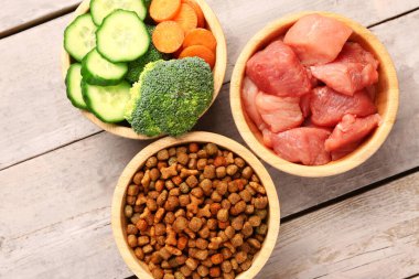 Kuru hayvan mamasıyla dolu kaseler, çiğ et ve hafif ahşap arka planda doğal ürünler, yakın plan.