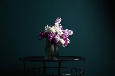 Koyu yeşil duvarın yanındaki masada güzel kokulu leylak çiçekleri.
