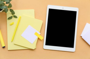 Turuncu arkaplan üzerine not defterleri ve yapışkan notlar içeren tablet