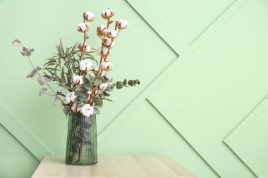 Pamuk filizi vazosu ve okaliptüs yeşil duvarın yanındaki açık ahşap masada.