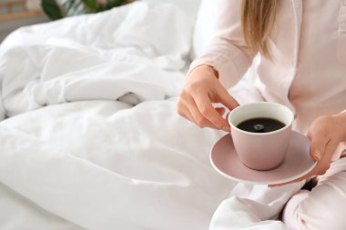 Bir kadın yatakta lezzetli bir fincan kahve ve çay tabağı tutuyor.