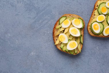 Lezzetli kızarmış ekmek, bıldırcın yumurtası, avokado ve mavi arka planda salatalık.