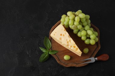 Lezzetli İsviçre peyniri ve siyah arka planda üzümlü ahşap tahta.