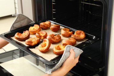Mutfaktaki fırından lezzetli Yorkshire pudingli fırın tepsisi alan kadın.