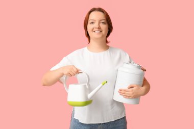 Sulama kabı ve pembe arka planda metalik kabıyla gülümseyen genç kadın.