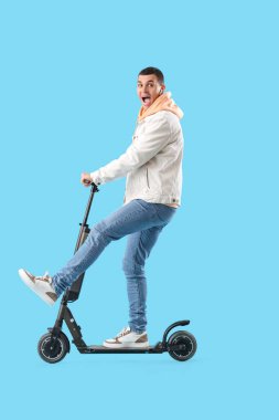 Mavi arka planda elektrikli scooter kullanan genç adam.