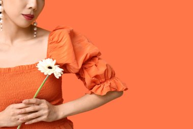 Turuncu arka planda beyaz gerbera çiçekli genç Asyalı kadın.