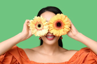 Yeşil arka planda Gerbera çiçekleri olan güzel bir Asyalı kadın.