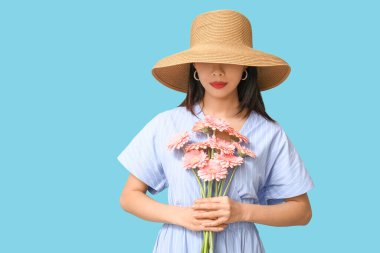 Mavi arka planda pembe Gerbera çiçekleri olan güzel bir Asyalı kadın.