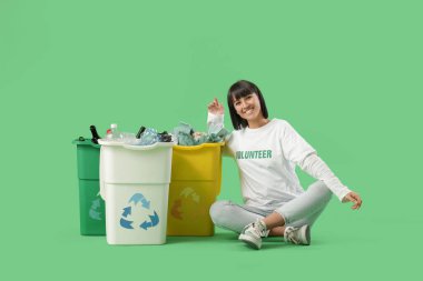 Yeşil arka planda çöp konteynırları olan genç bir kadın. Geri dönüşüm kavramı