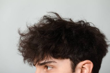 Gri arka planda koyu renk saçlı genç adam, yakın plan.