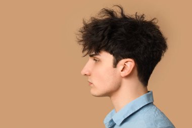 Bej arka planda koyu renk saçlı genç bir adam.