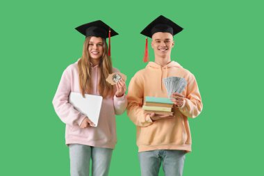 Mezuniyet şapkalı genç öğrenciler domuz kumbarası, kitaplar, dizüstü bilgisayarlar ve yeşil arka planda para. Eğitim için tasarruf kavramı