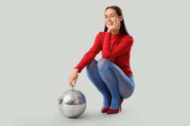 Gri arka planda oturan, disko topuyla mutlu, genç, modaya uygun bir kadın.