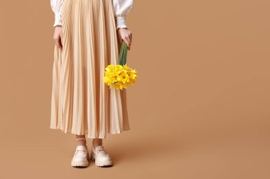 Bej arka planda güzel narsisli çiçeklerle dolu buketi olan güzel genç bir kadın. Yakın plan.