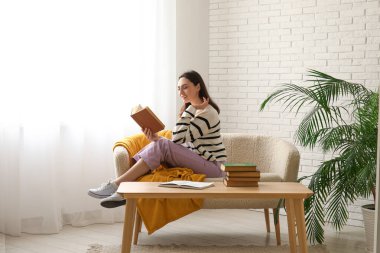 Young woman sitting on sofa and reading book in living room